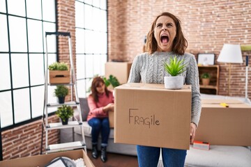 Sticker - Mother and daughter moving to a new home holding cardboard box angry and mad screaming frustrated and furious, shouting with anger looking up.