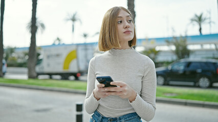 Wall Mural - Young blonde woman using smartphone with serious expression at street