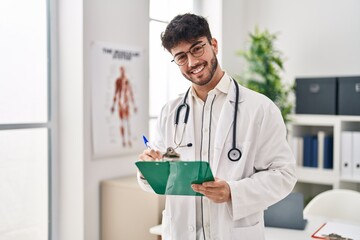 Poster - Young hispanic man wearing doctor uniform writing medical report at clinic