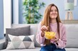 © Krakenimages.com - Young caucasian woman eating chips potatoes sitting on sofa at home
