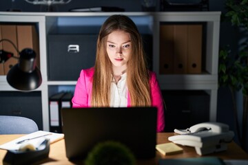 Poster - Young caucasian woman working at the office at night relaxed with serious expression on face. simple and natural looking at the camera.