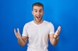 © Krakenimages.com - Young caucasian man standing over blue background celebrating crazy and amazed for success with arms raised and open eyes screaming excited. winner concept
