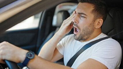 Wall Mural - Young hispanic man tired driving car yawning at street