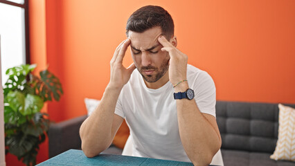 Poster - Young hispanic man suffering for headache sitting on table at dinning room