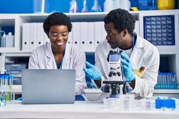 Canvas Print - African american man and woman scientists using laptop and microscope at laboratory