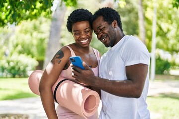 Poster - African american man and woman couple holding yoga mat using smartphone at park