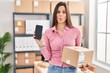 Young hispanic woman working at small business ecommerce showing smartphone screen making fish face with mouth and squinting eyes, crazy and comical.