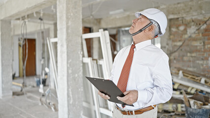 Sticker - Senior grey-haired man architect holding clipboard looking around at construction site