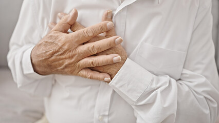 Poster - Senior grey-haired man sitting on sofa suffering heart attack at home