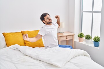 Wall Mural - Young hispanic man waking up sitting on bed at bedroom