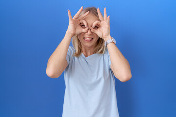 Canvas Print - Young caucasian woman wearing casual blue t shirt doing ok gesture like binoculars sticking tongue out, eyes looking through fingers. crazy expression.