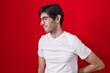 © Krakenimages.com - Young hispanic man standing over red background suffering of backache, touching back with hand, muscular pain