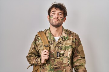 Poster - Hispanic young man wearing camouflage army uniform relaxed with serious expression on face. simple and natural looking at the camera.