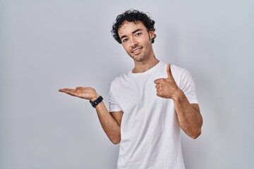 Poster - Hispanic man standing over isolated background showing palm hand and doing ok gesture with thumbs up, smiling happy and cheerful