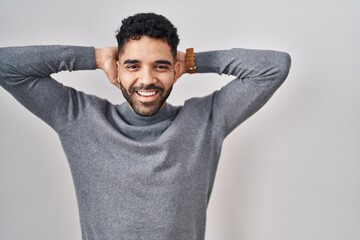 Wall Mural - Hispanic man with beard standing over white background relaxing and stretching, arms and hands behind head and neck smiling happy