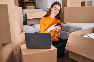 Poster - Young caucasian woman using laptop and smartphone at new home