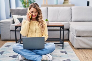 Canvas Print - Young woman using laptop and talking on smartphone at home