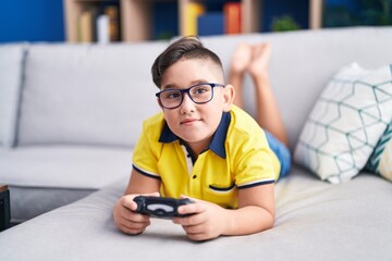 Canvas Print - Young hispanic kid playing video game holding controller on the sofa smiling looking to the side and staring away thinking.