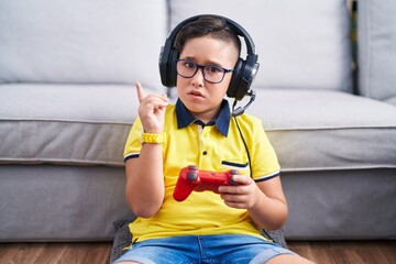 Sticker - Young hispanic kid playing video game holding controller wearing headphones pointing aside worried and nervous with forefinger, concerned and surprised expression