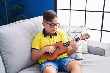 Sticker - Adorable hispanic boy playing ukulele sitting on sofa at home