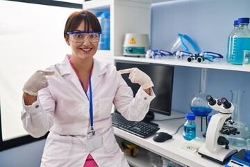 Poster - Young brunette woman working at scientist laboratory looking confident with smile on face, pointing oneself with fingers proud and happy.