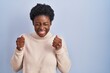 © Krakenimages.com - African american woman standing over blue background excited for success with arms raised and eyes closed celebrating victory smiling. winner concept.