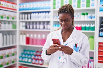 Wall Mural - African american woman pharmacist using smartphone working at pharmacy