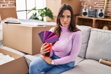 Poster - Young brunette woman moving to a new home choosing wall painting thinking attitude and sober expression looking self confident