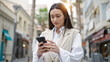 © Krakenimages.com - Young beautiful hispanic woman using smartphone with serious expression at street
