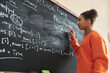 © Seventyfour - Side view portrait of black teenage girl writing on blackboard in school classroom, copy space