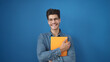 © Krakenimages.com - Young hispanic man smiling confident holding book over isolated blue background