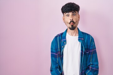 Wall Mural - Young hispanic man with beard standing over pink background making fish face with lips, crazy and comical gesture. funny expression.