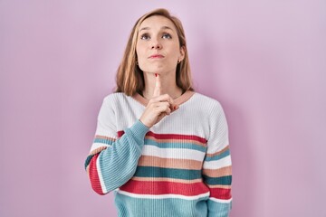 Wall Mural - Young blonde woman standing over pink background thinking concentrated about doubt with finger on chin and looking up wondering