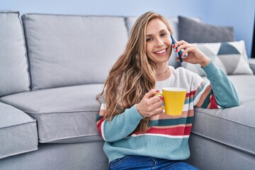 Poster - Young blonde woman talking on smartphone drinking coffee at home