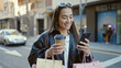 © Krakenimages.com - Young beautiful hispanic woman using smartphone holding shopping bags and coffee at street