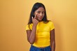 Young indian woman standing over yellow background pointing to the eye watching you gesture, suspicious expression