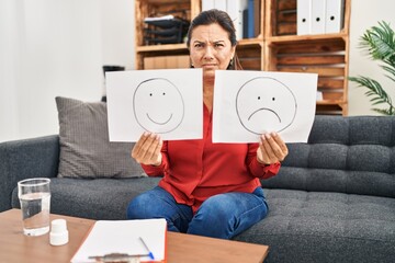 Poster - Middle age hispanic woman working on depression holding sad to happy emotion paper clueless and confused expression. doubt concept.