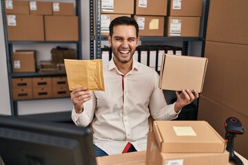 Poster - Young hispanic man with beard working at small business ecommerce holding delivery packages smiling and laughing hard out loud because funny crazy joke.