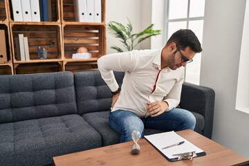 Canvas Print - Young hispanic man with beard working at consultation office suffering of backache, touching back with hand, muscular pain