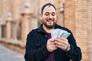 Wall Mural - Young hispanic man smiling confident counting dollars at street