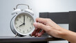 © Summer Paradive - Time management concept. Male hand placing white alarm clock on the table.