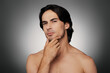 © gstockstudio - Portrait of young shirtless man holding hand on chin against grey background
