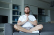 © Евгений Шемякин - Young man with a beard alone at home, relax in living room ,sitting on the couch and meditating in the lotus position, in casual clothes