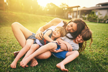 mother, children and hug playing on grass for fun bonding in the sun outside their house in nature. 