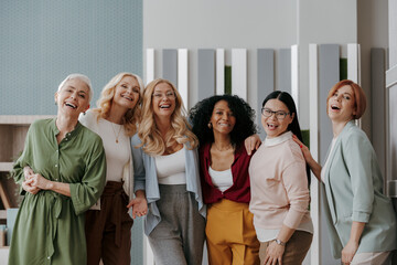 Wall Mural - Group of happy mature women looking at camera while standing in the office together