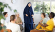 Friendly young Asian woman in traditional Muslim dress with chador on head participating in adult educational course talking with interest to classmates sitting 