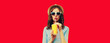 Leinwandbild Motiv Portrait of stylish young woman drinking fresh juice wearing summer straw hat, sunglasses on red background
