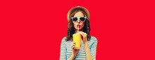 Portrait Of Stylish Young Woman Drinking Fresh Juice Wearing Summer Straw Hat, Sunglasses On Red Background