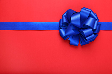 Blue ribbon with bow on red background, top view. Space for text