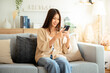 © Monster Ztudio - Happy young asian woman relax on comfortable couch at home texting messaging on smartphone, smiling girl use cellphone chatting, browse wireless internet on gadget, shopping online from home